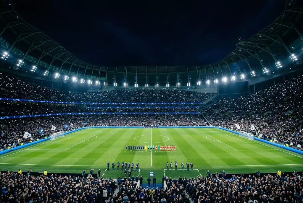 A football stadium at night with the pitch brightly lit and thousands of spectators filling every tier during a World Cup evening kickoff